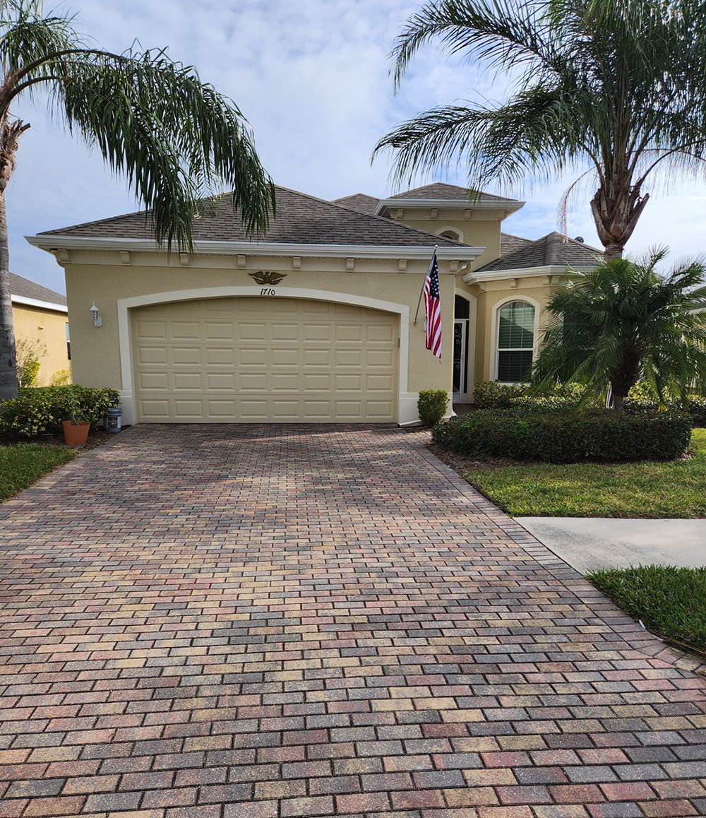 A brick driveway leading to a house with a garage and palm trees